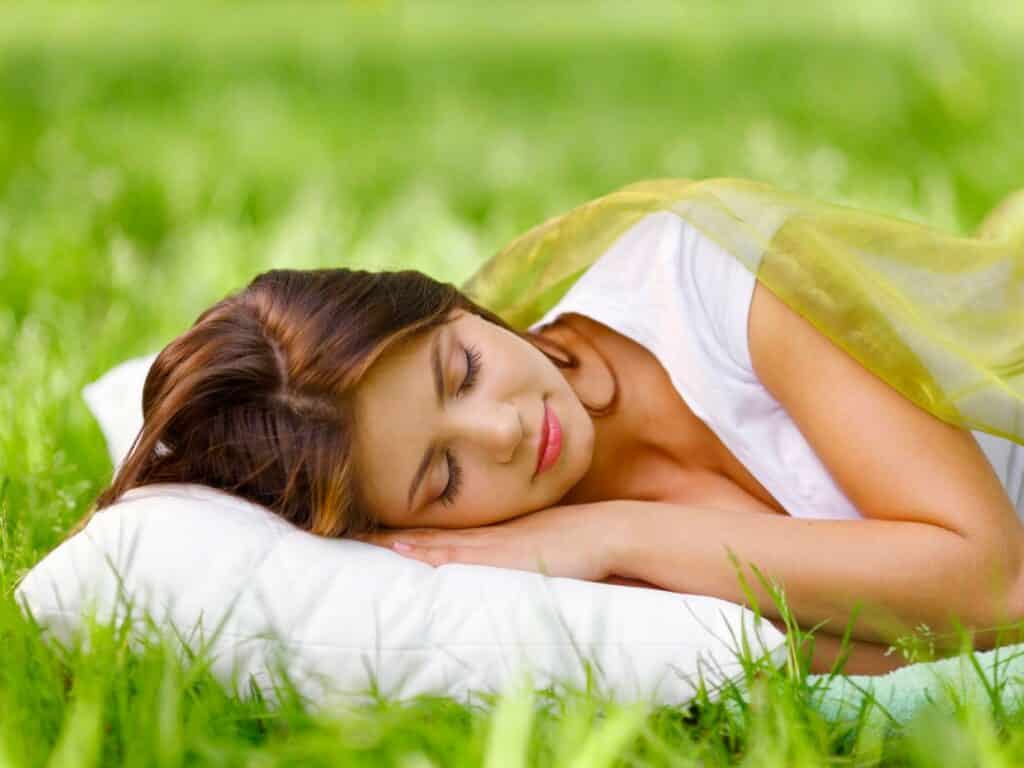 Woman sleeping on a pillow on grass, representing Secrets to Sleeping Well