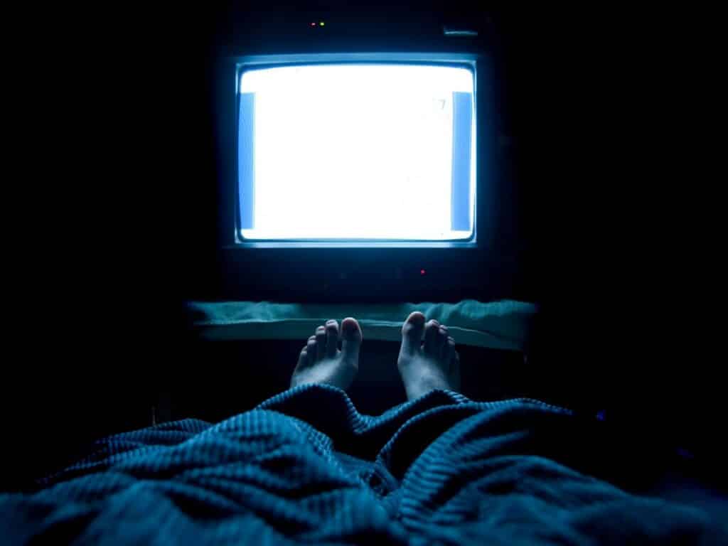 Person in bed watching TV. Why You Can't Sleep.