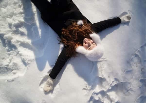 Girl laying in the snow with a smile on her face, representing how to Have less frazzle and more fun this holiday