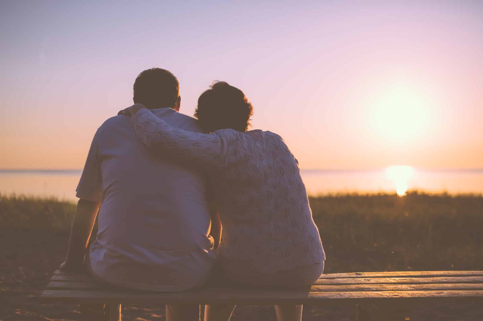 Couple sitting on a bench, looking at the sunset working on healing their marriage bond