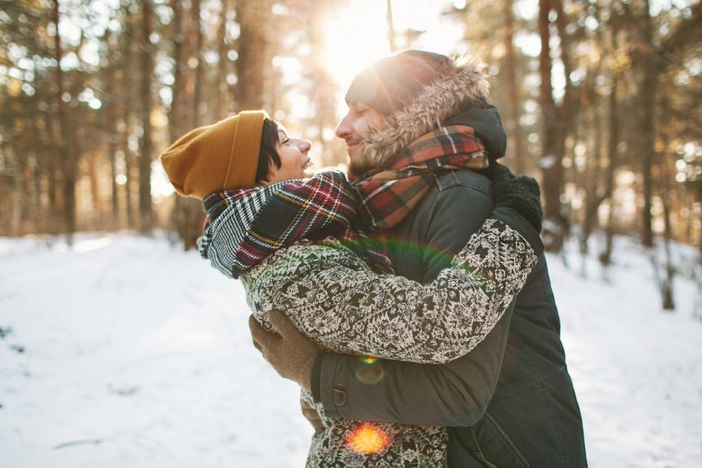 couple embracing in the snow with sun setting through the trees representing How to Find "The One" This Year