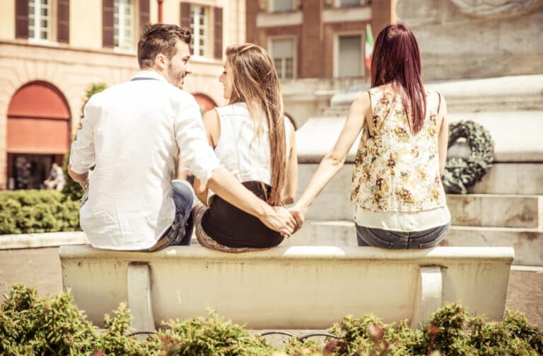 Couple sitting outside. Man holding hands with another woman representing recovering from infidelity.