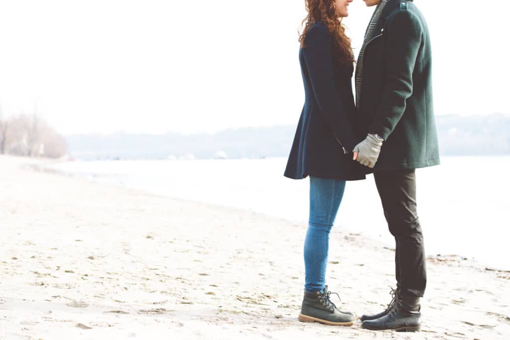 Couple holding hands on the beach wondering if they have relationship compatibility.