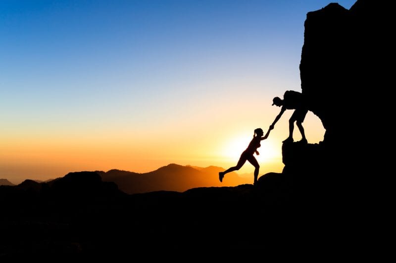 Person pulling up another person on a hike. Daring to trust again.