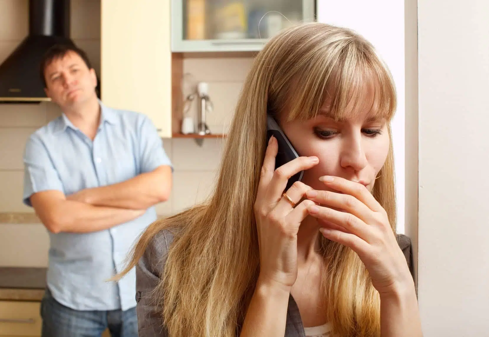 Woman on phone with man watching behind her representing telltale signs of an emotional affair