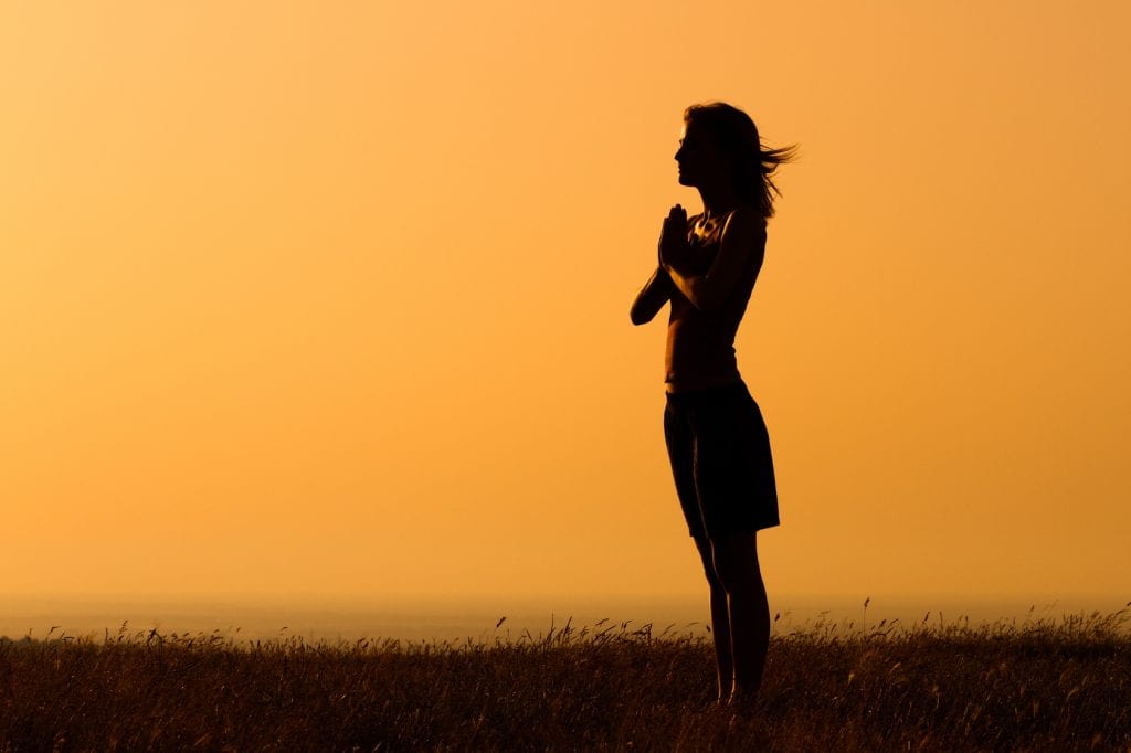 Woman outside with hands together practicing How to feel happier instantly.