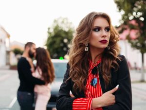 ex kissing another woman in the background. woman looking the other way with her arms crossed. How to stop obsessing about your ex's new relationship.