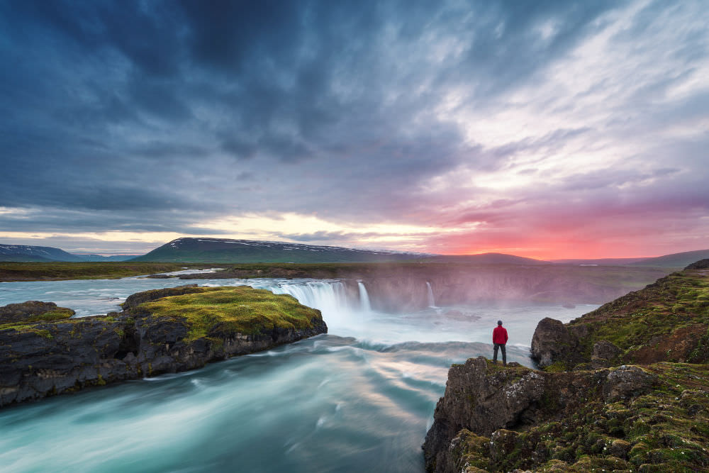 Person standing at a beautiful waterfall ready to break free from what's holding them back from success
