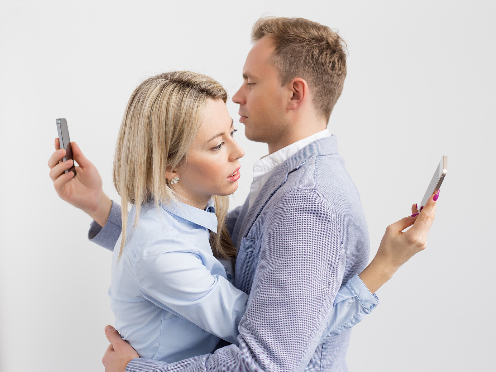 Couple embracing, looking at phones instead of each other navigating technology and relationships.