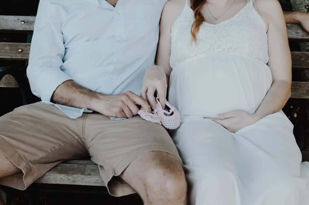 Expecting couple holding tiny baby shoes learning how to manage relationship stress during pregnancy.