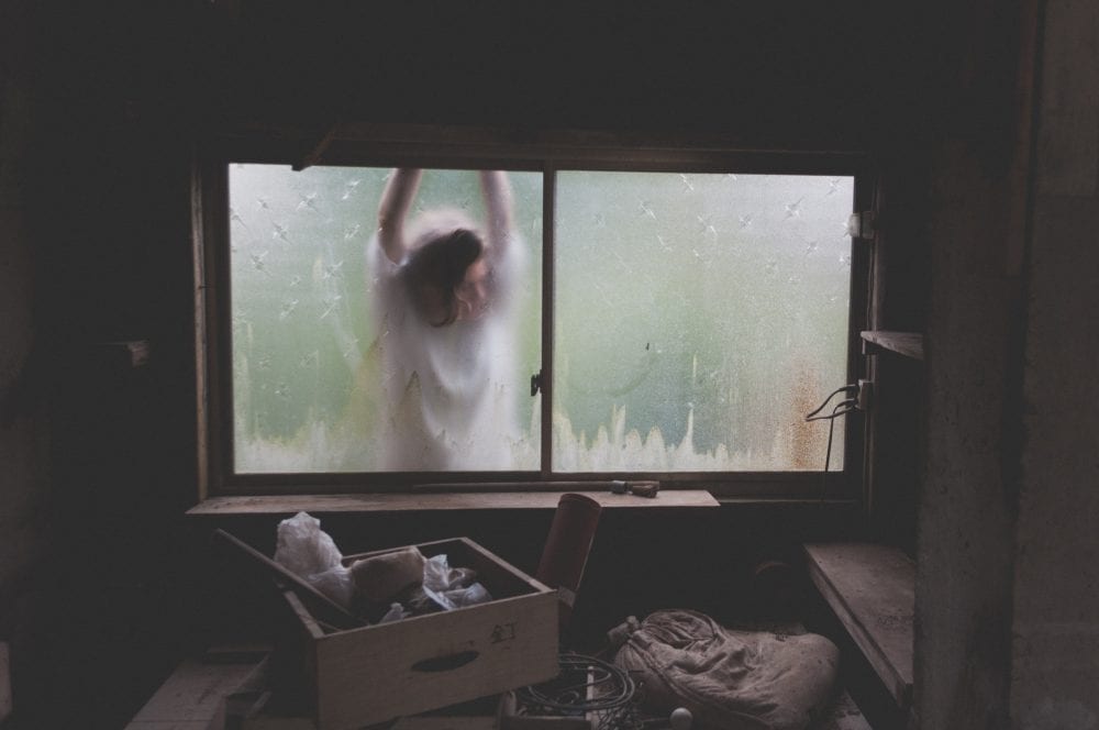 Girl leaning against backlit window looking into a dark room, representing how to Stop Self-Sabotage this Year