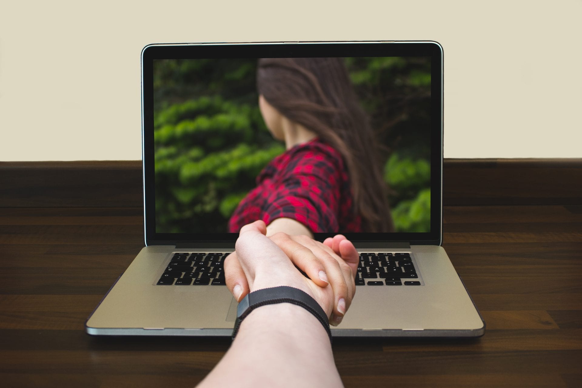 Couple holding hands through computer in an online relationship