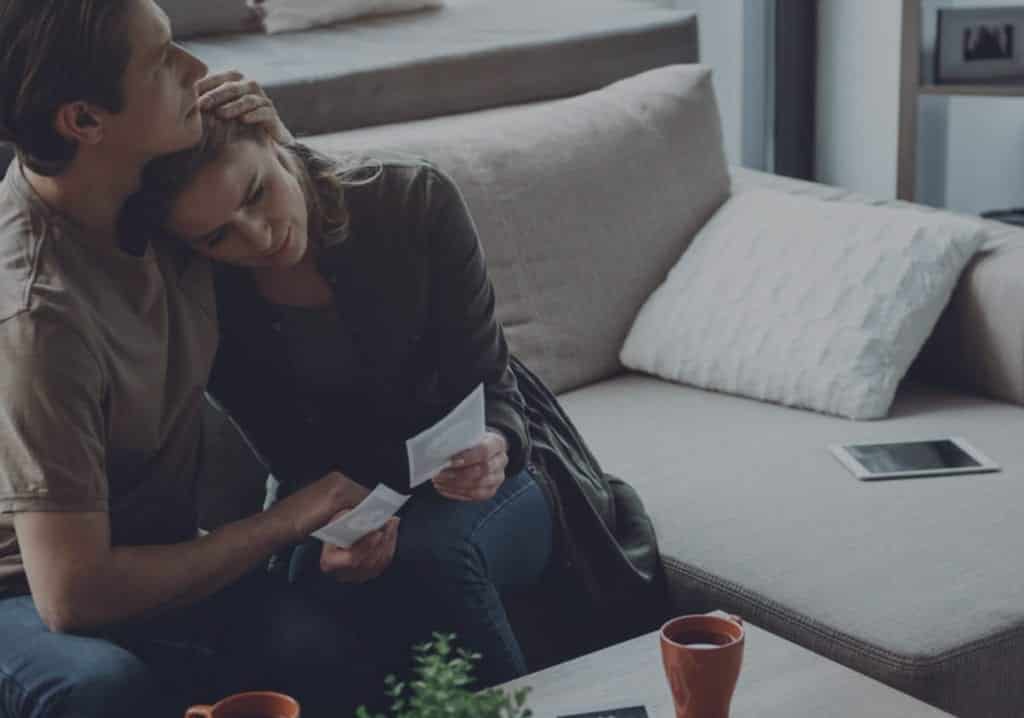 Man and woman sitting on the couch, embracing getting through hard times together.