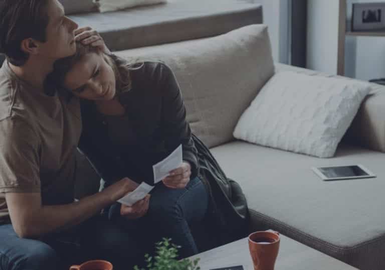Man and woman sitting on the couch, embracing getting through hard times together.