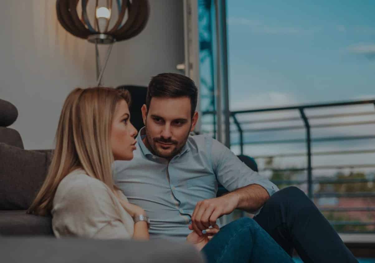 Couple sitting on a couch. Man is turned towards woman, listening to what she is saying about how to stop Fixing a relationship and Start Listening.