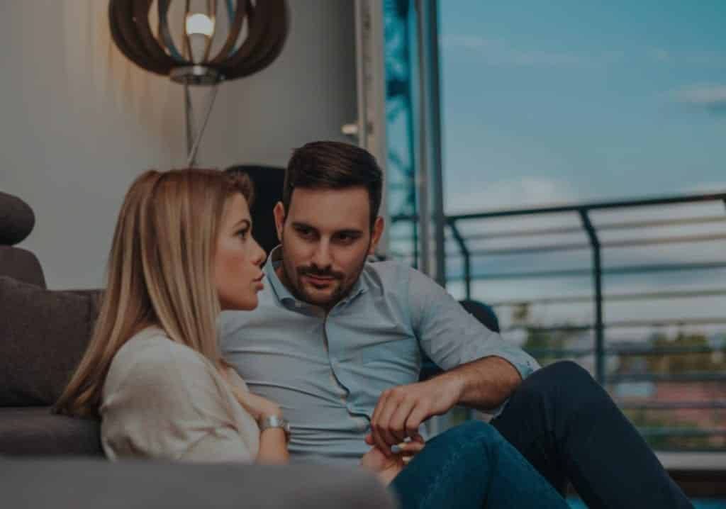 Couple sitting on a couch. Man is turned towards woman, listening to what she is saying about how to stop Fixing a relationship and Start Listening.