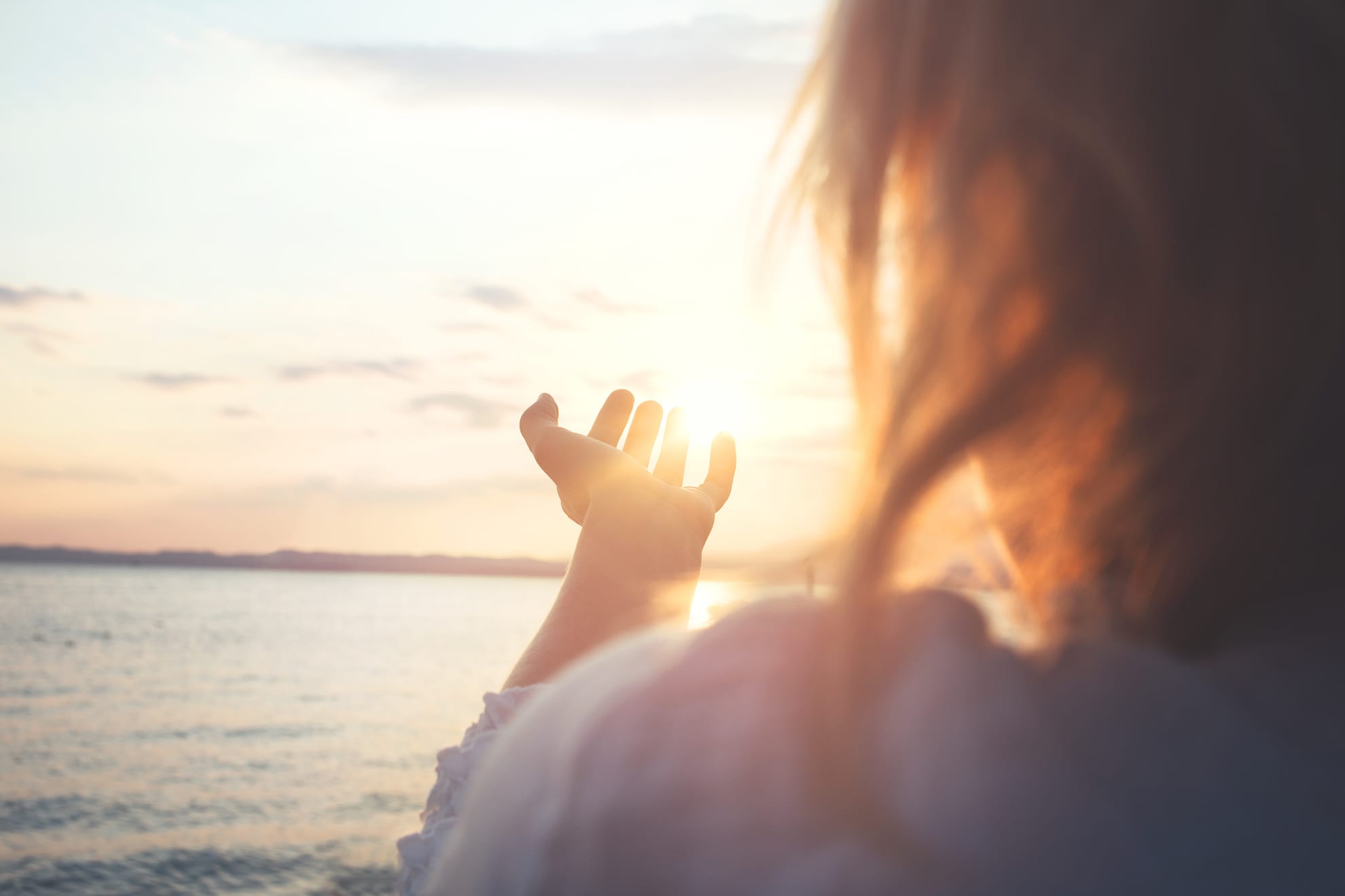 woman holding hand out toward sunrise over ocean thinking about self discovery