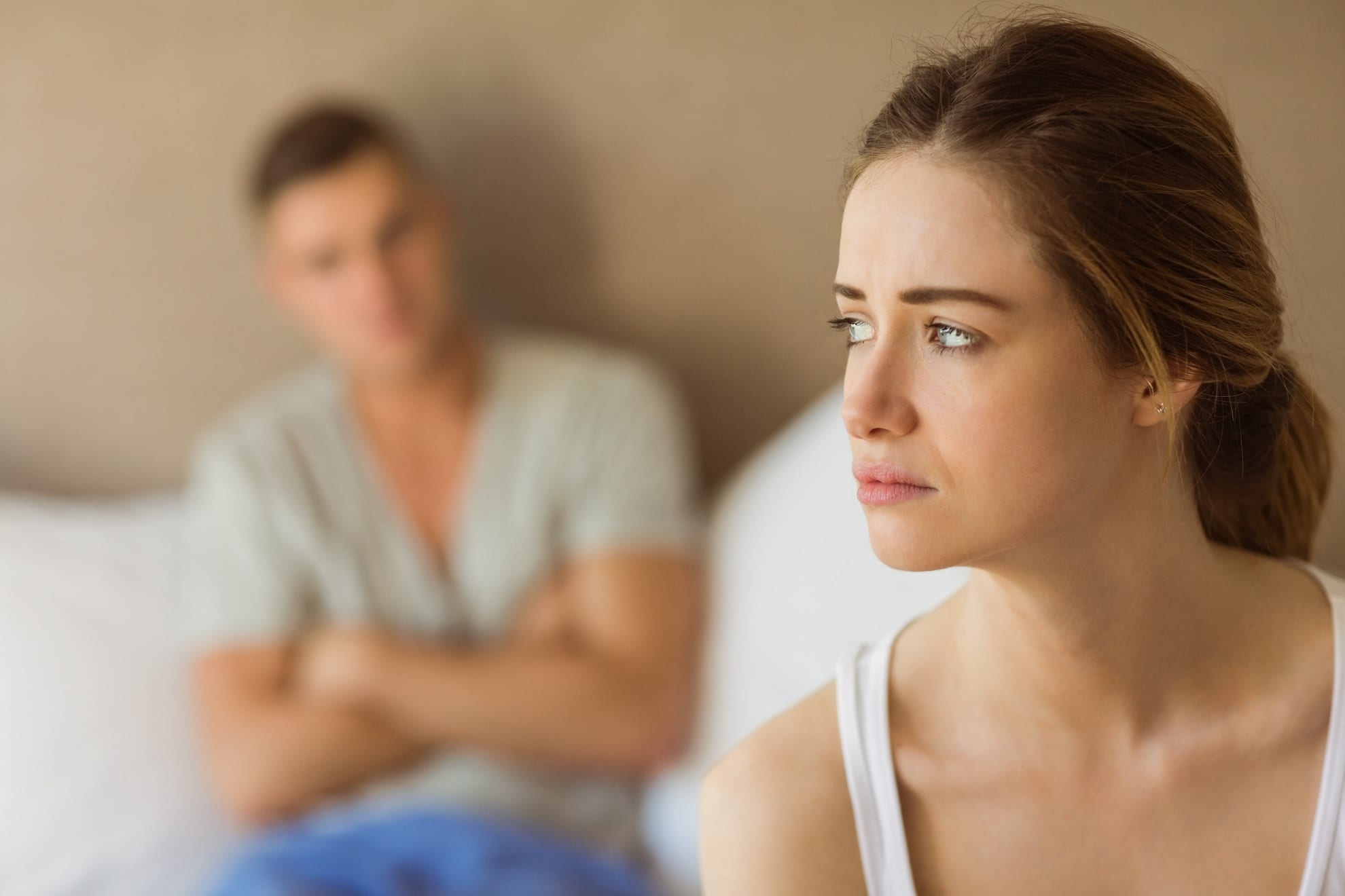 Woman looking sullen in the foreground. Man with his arms crossed in the background representing When Do You Need Marriage Counseling?