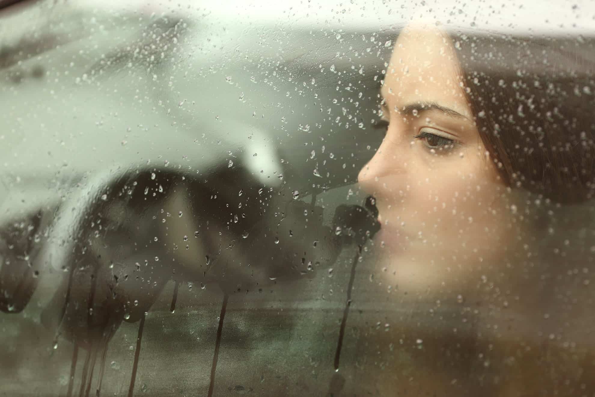 Woman looking out of a rainy window looking for help for getting out of a funk.