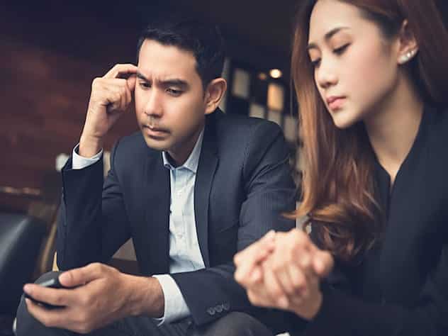 Couple sitting together looking down. Help! My job is ruining our relationship.