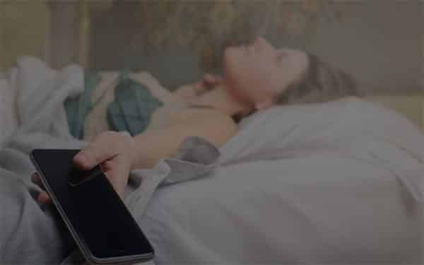 Woman in bed with phone in her hand looking distressed dealing with new relationship anxiety