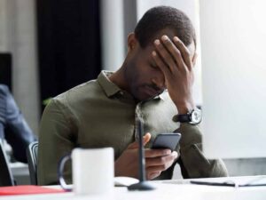 Man looking at his phone with his hand on his forehead feeling stuck in a toxic workplace