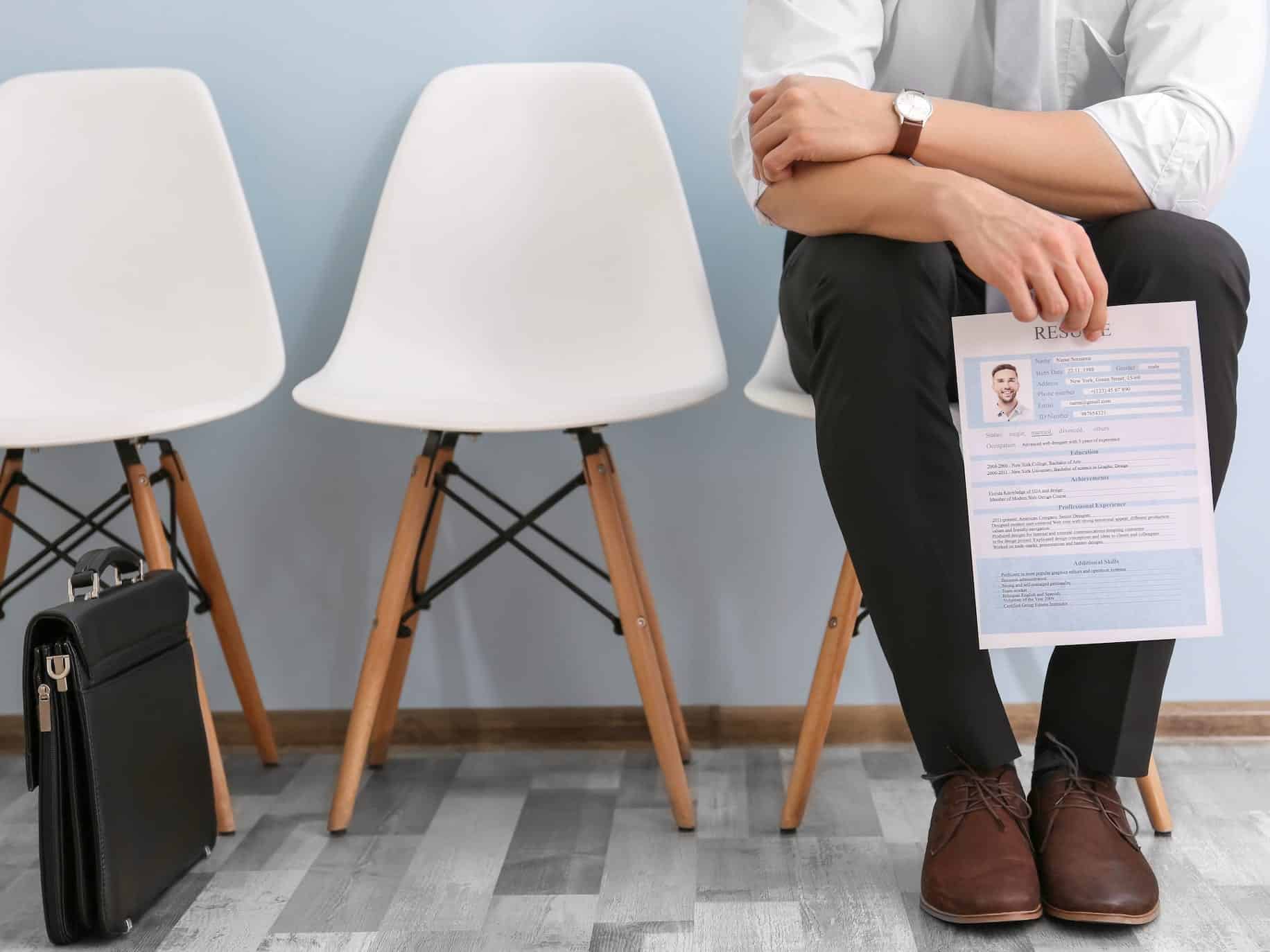 Man sitting in a waiting room with a briefcase and a resume trying to find a new job.