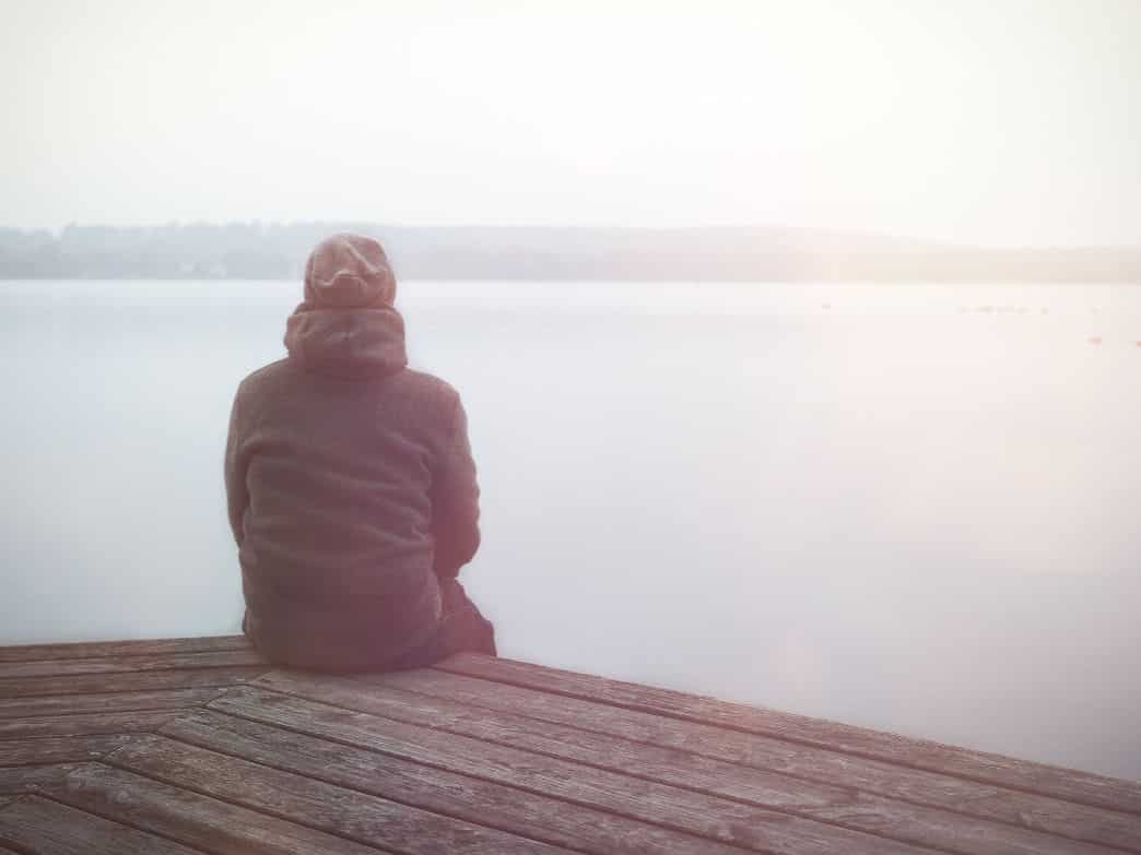 Man sitting on a dock, looking out over the water. Managing The Late-Winter Blues.