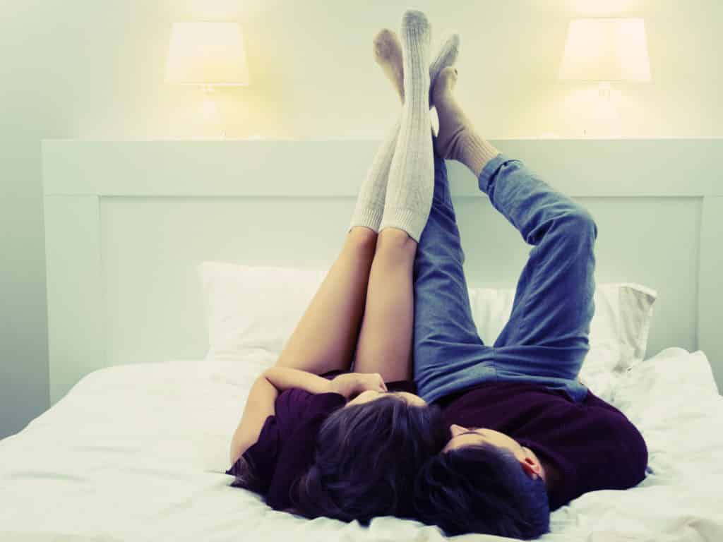 Couple laying down on a bed with their feet up in the air. are you compatible?