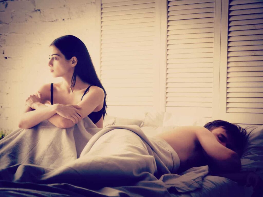 Woman sitting up in bed, man sleeping. Should You Have Sex With Your Ex.