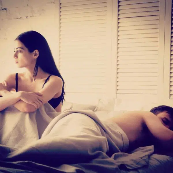 Woman sitting up in bed, man sleeping. Should You Have Sex With Your Ex.