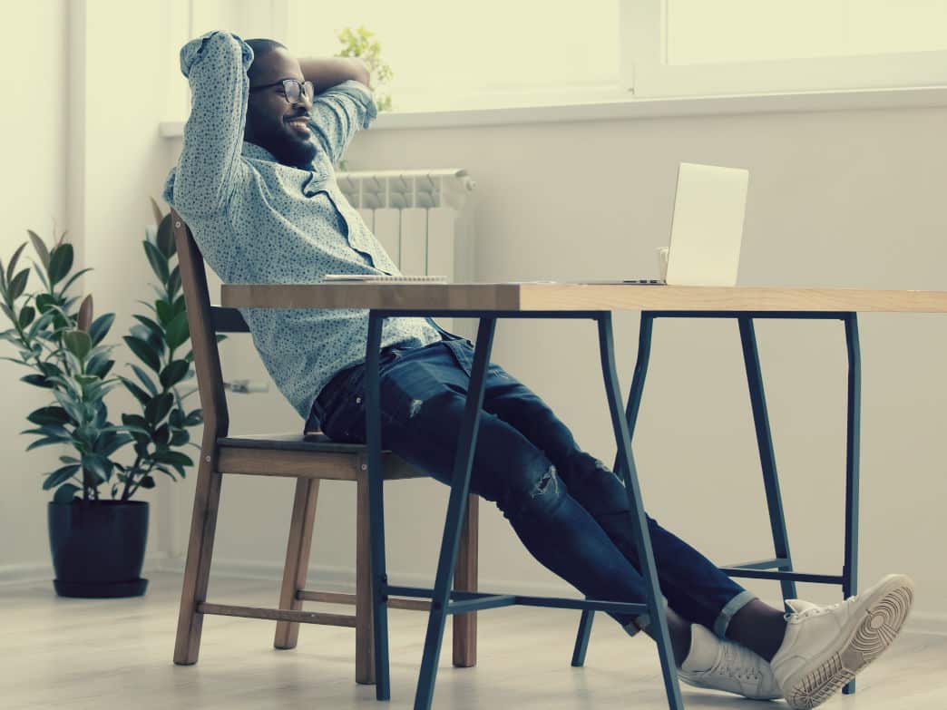 Person sitting back in a chair at a desk. How To Get Ahead At Work.
