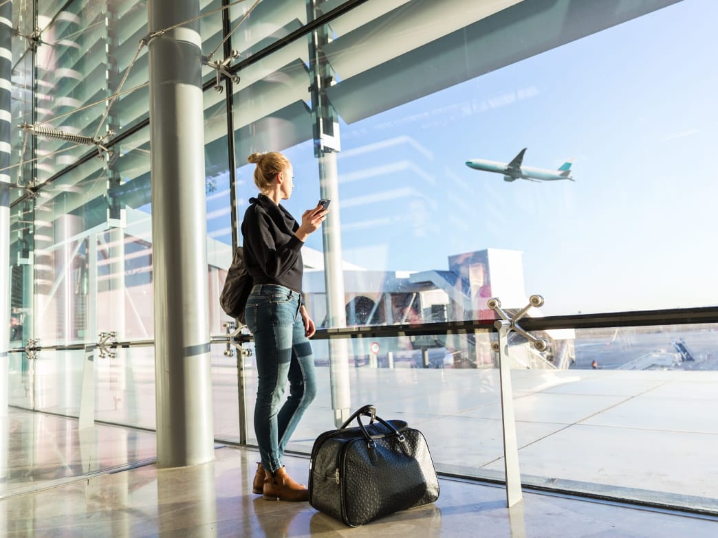 Woman at the airport, looking at a plane taking off. 3 Quick Tips for Self-Care While Traveling For Work.