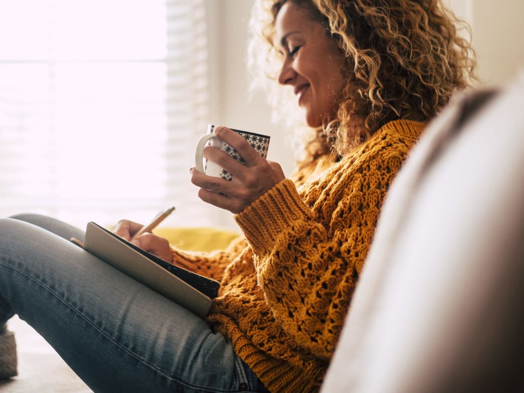 Woman sitting on a couch with a notepad and coffee representing Self care is not selfish.