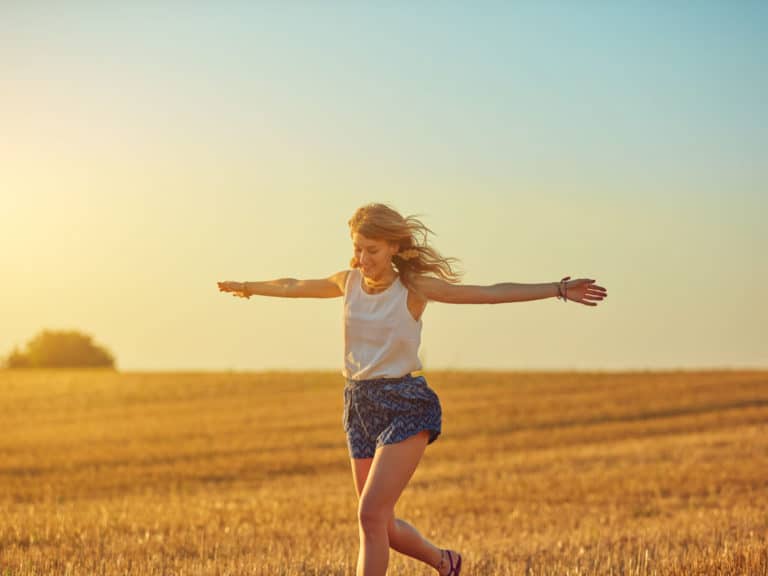 Joyful woman in an open field with arms out to side and wind in her hair representing Invest in Yourself