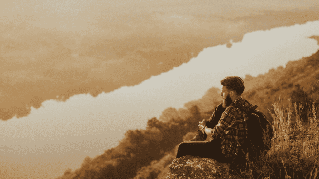 Man sitting on a cliff, looking at the view. How to achieve your most ambitious goals.