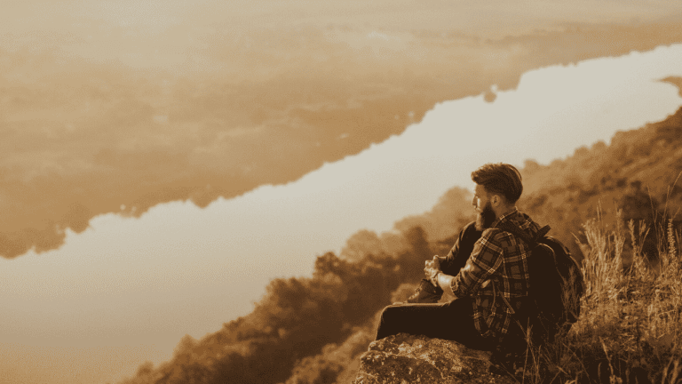 Man sitting on a cliff, looking at the view. How to achieve your most ambitious goals.