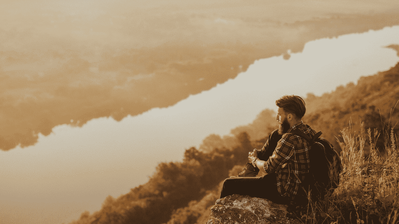 Man sitting on a cliff, looking at the view. How to achieve your most ambitious goals.