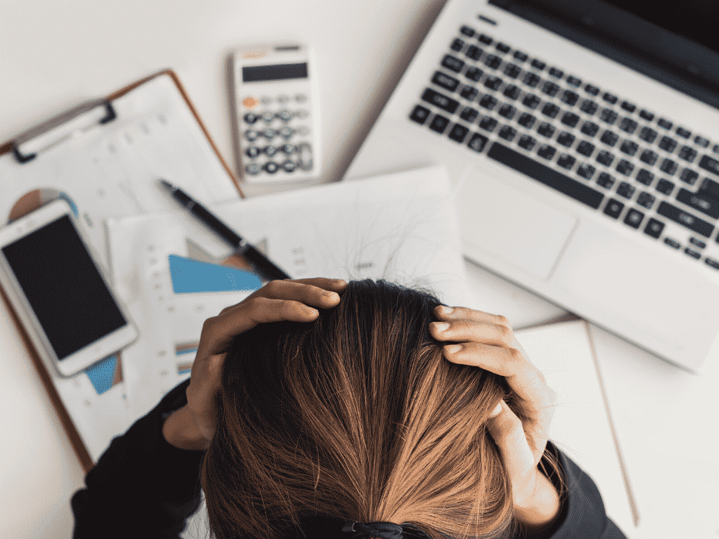 Woman staring down at her desk with her hands on top of her head. Coping with job loss.