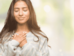 Woman with hands over heart looking satisfied and happy representing being honest with yourself.