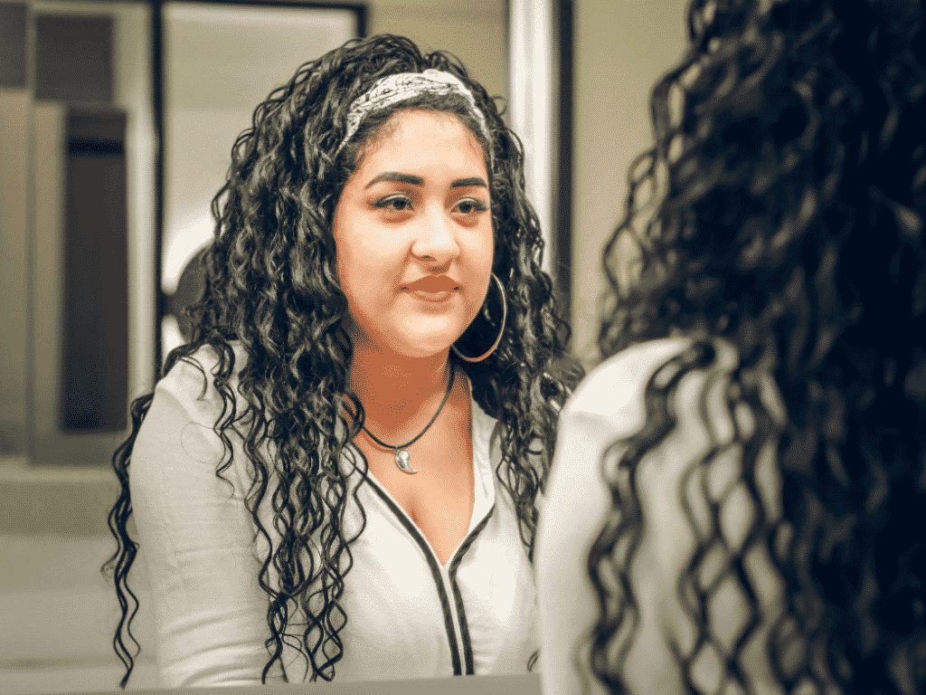 Woman looking at her reflection in the mirror representing you are good enough.