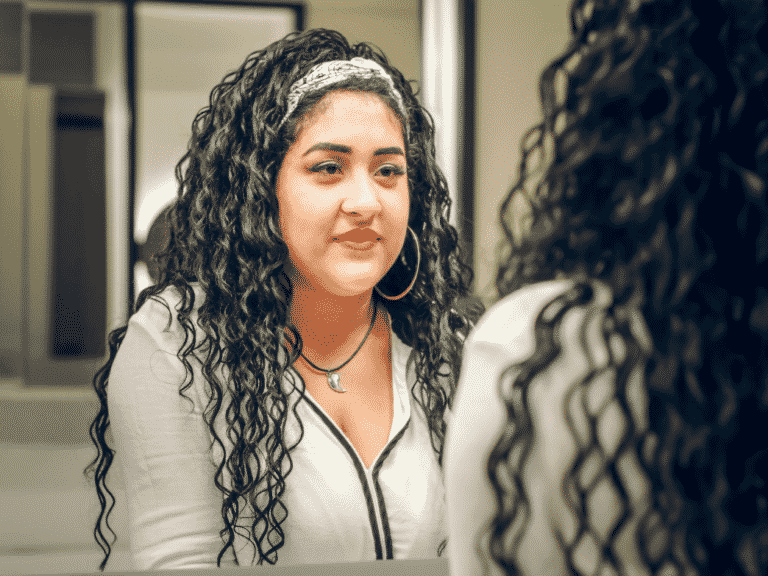 Woman looking at her reflection in the mirror representing you are good enough.
