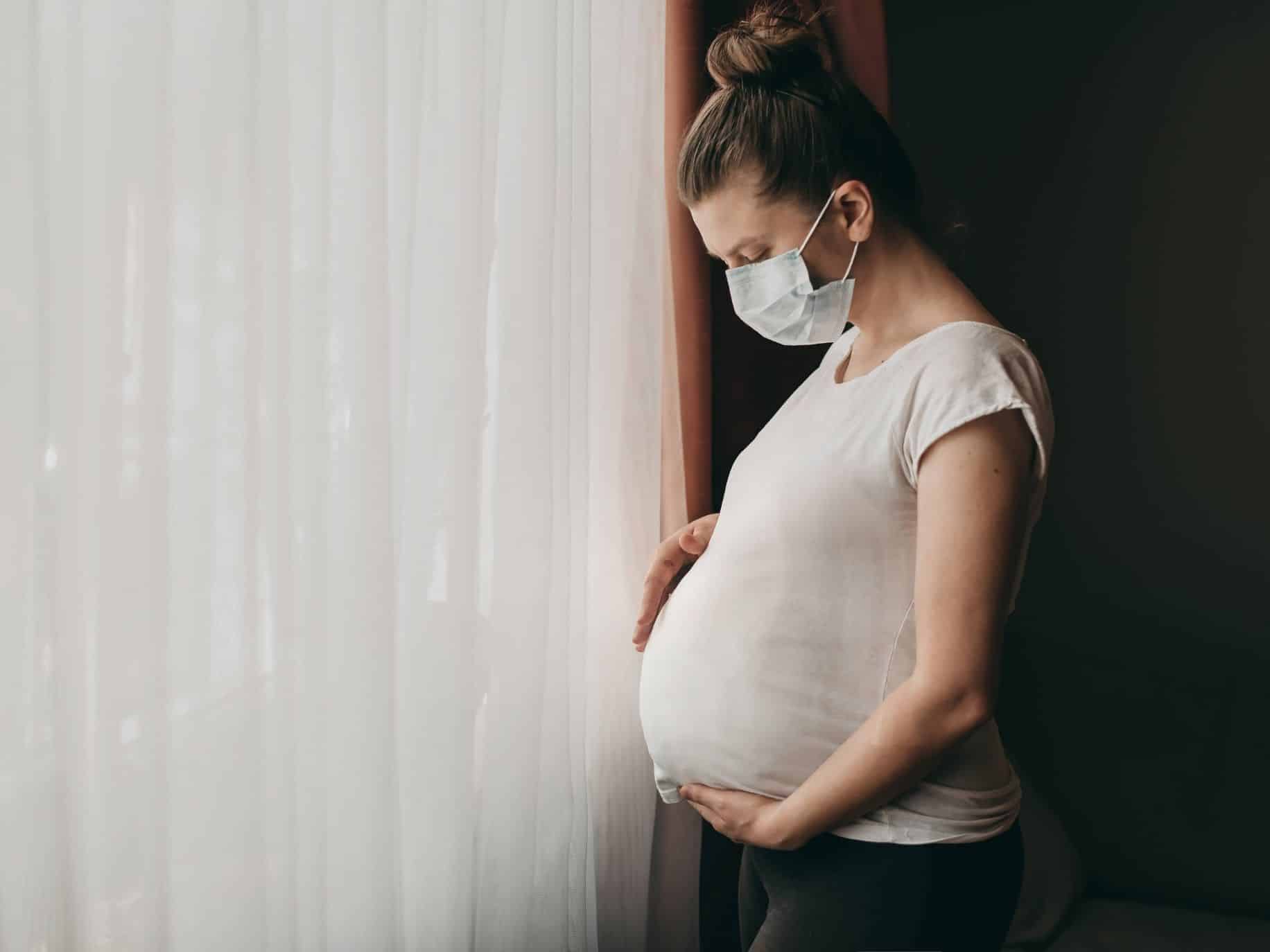 Mother looking down at pregnant belly. Expecting During an Unexpected Time Pandemic Pregnancy