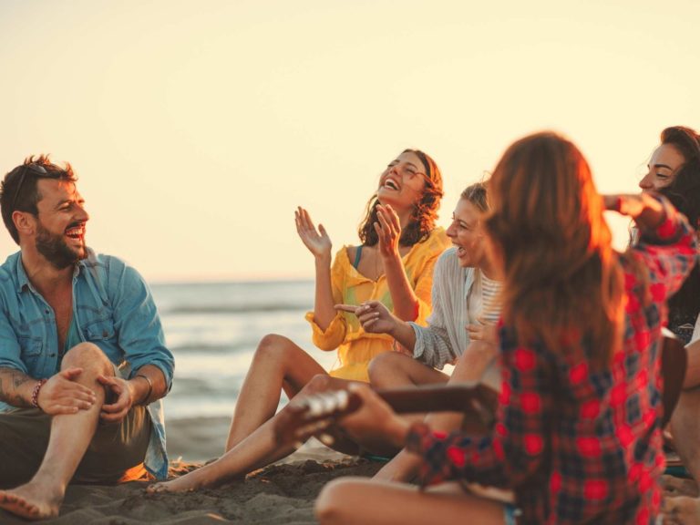 Circle of friends sitting together at the beach representing Build Confidence and Charisma.