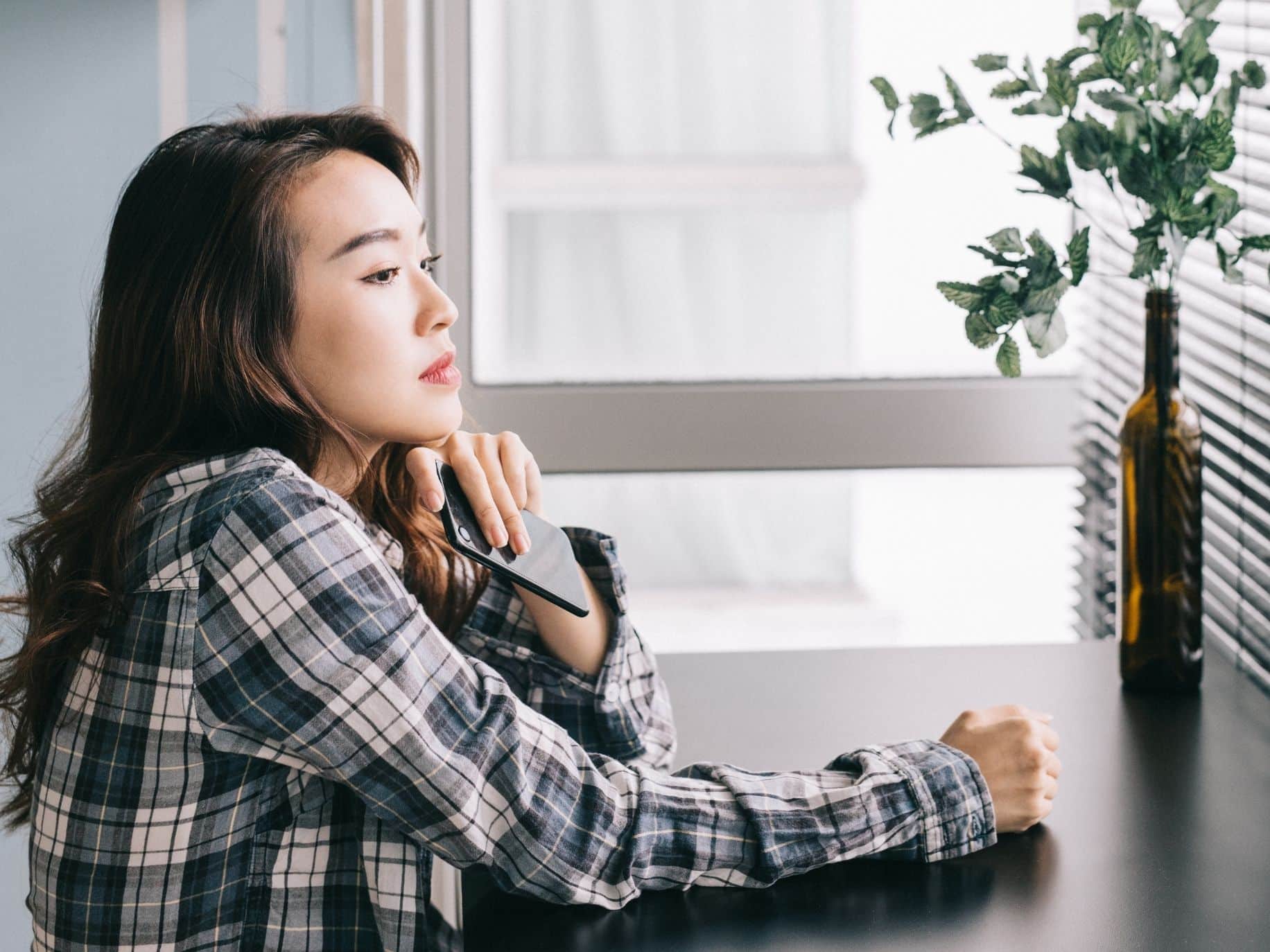 Woman sitting at a table with her phone in her hand. how to avoid ghosting in a relationship.