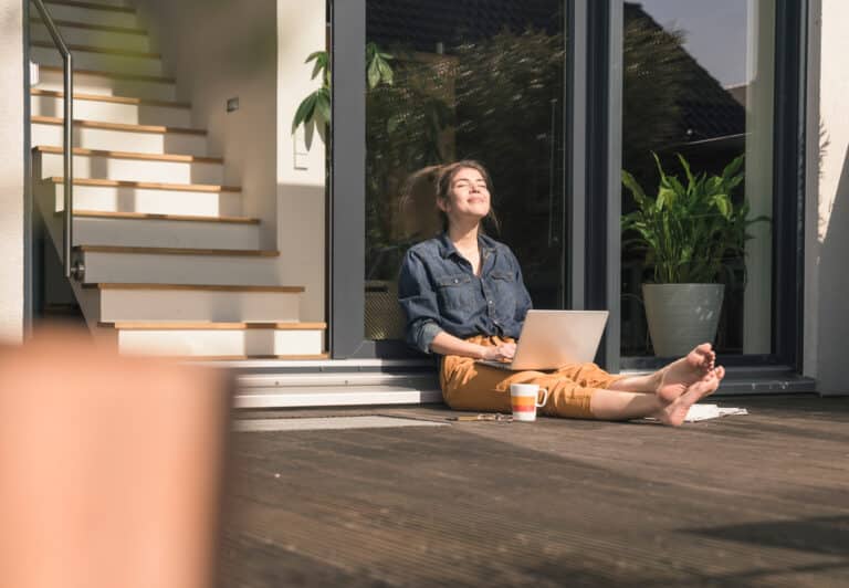 Young woman with closed eyes sitting on terrace at home with laptop