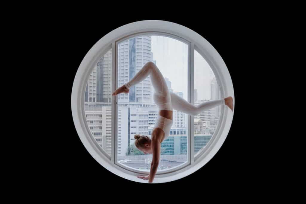 Athletic woman doing yoga in window, representing question of life coach insurance.