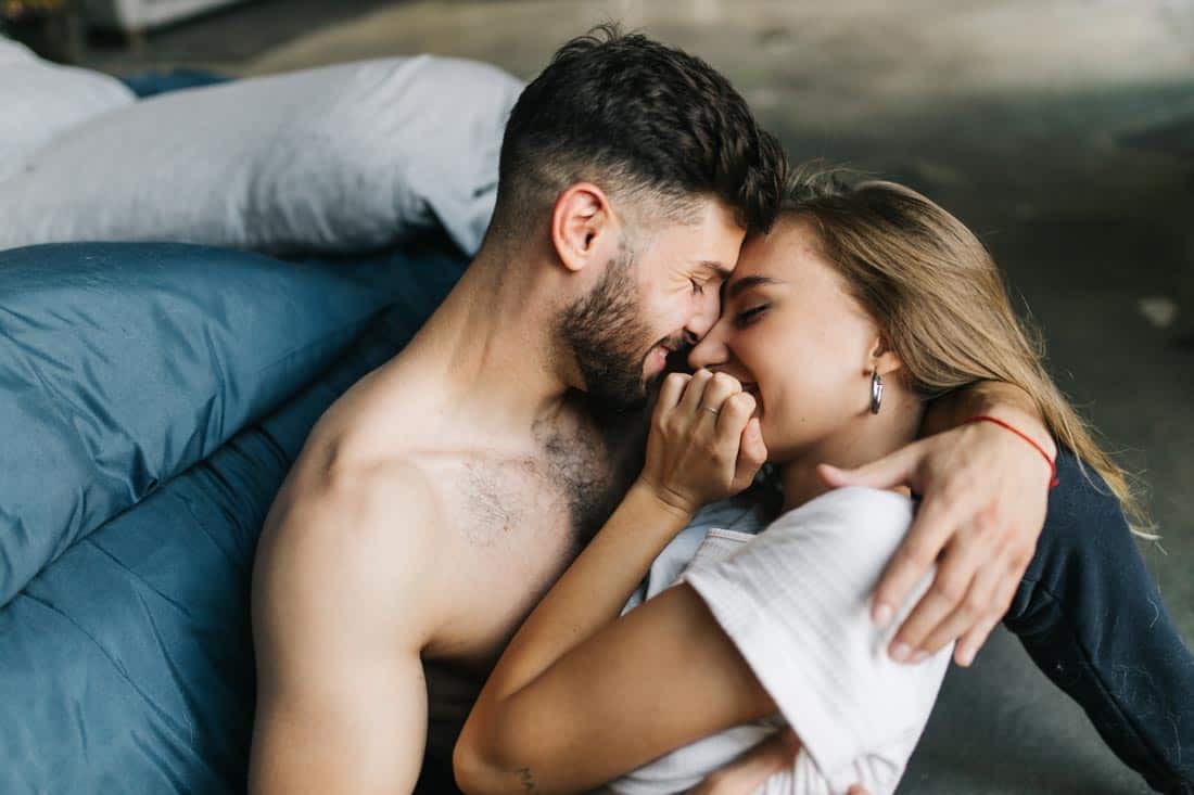 A man holds a woman lying in his lap, face to face in a bed.