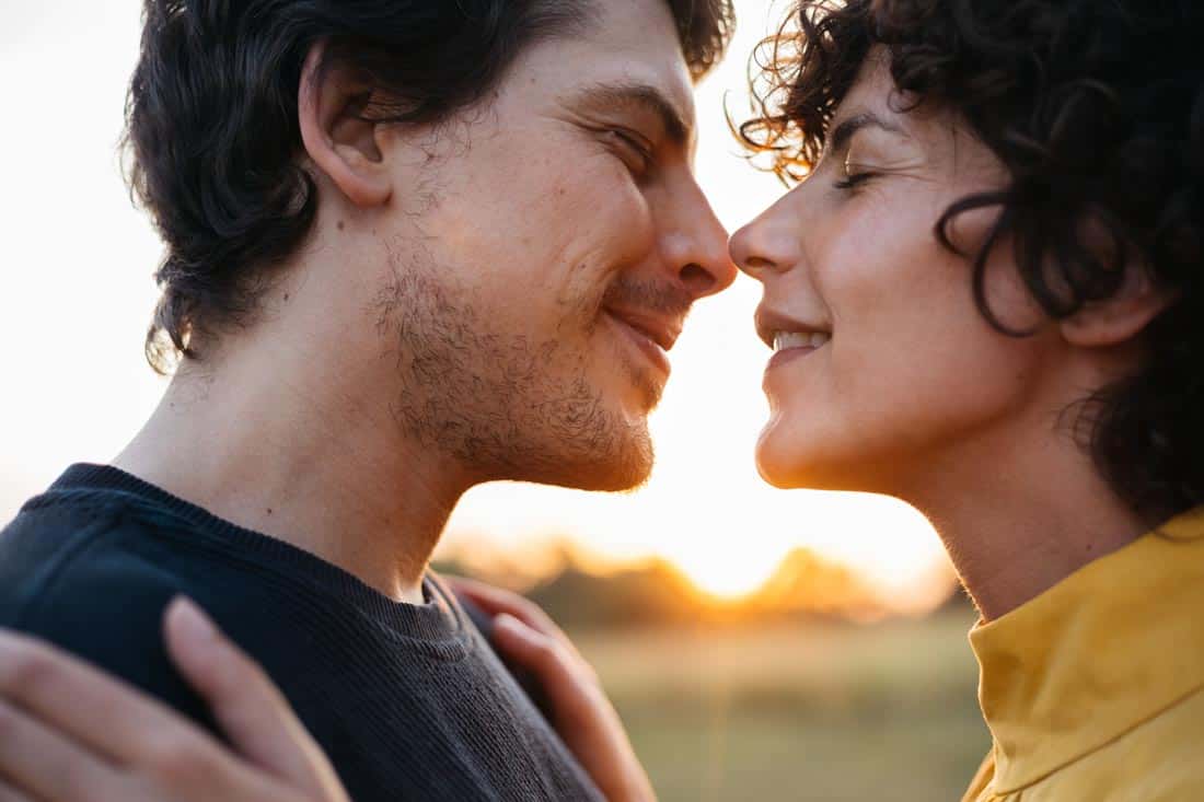 Man and woman touching noses in front of a sunset.