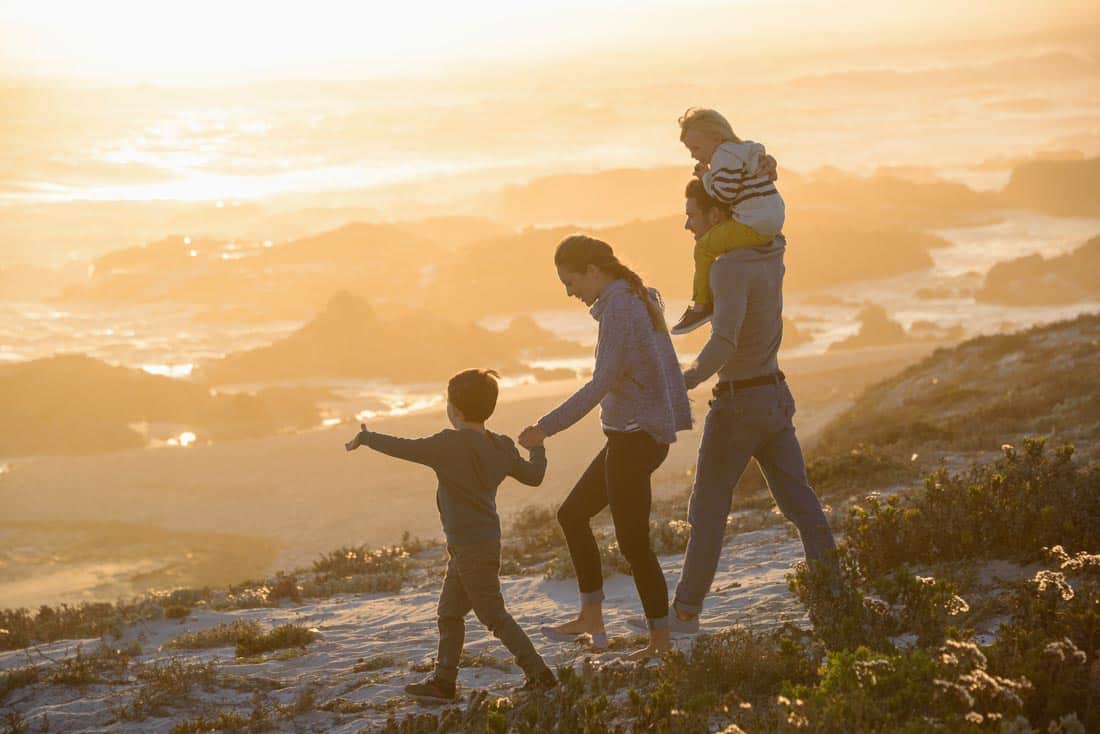 Family walking on cliffside at sunset